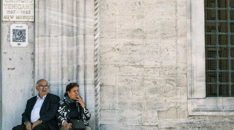 Senior couple sitting by the New Mosque in Eminönü, Istanbul, reflecting a moment of leisure.