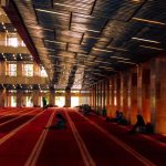 Stunning interior of a grand mosque with people praying on red carpet.