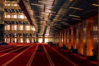 Stunning interior of a grand mosque with people praying on red carpet.