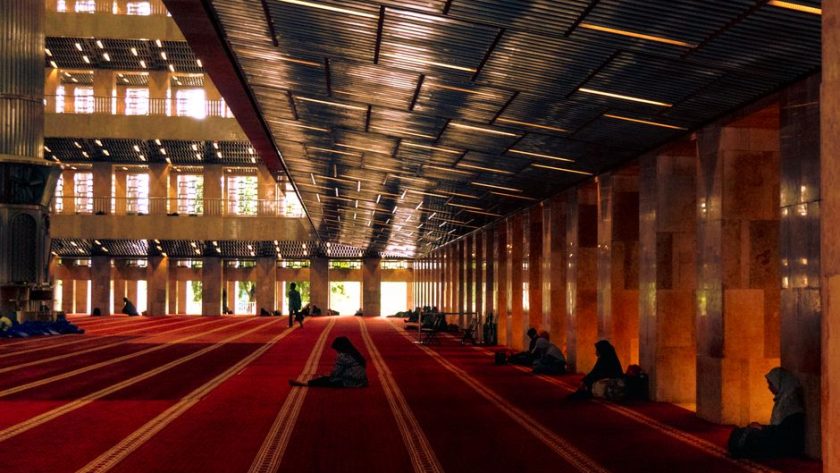 Stunning interior of a grand mosque with people praying on red carpet.