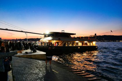 Ferry with lights sailing at dusk near a crowded dock