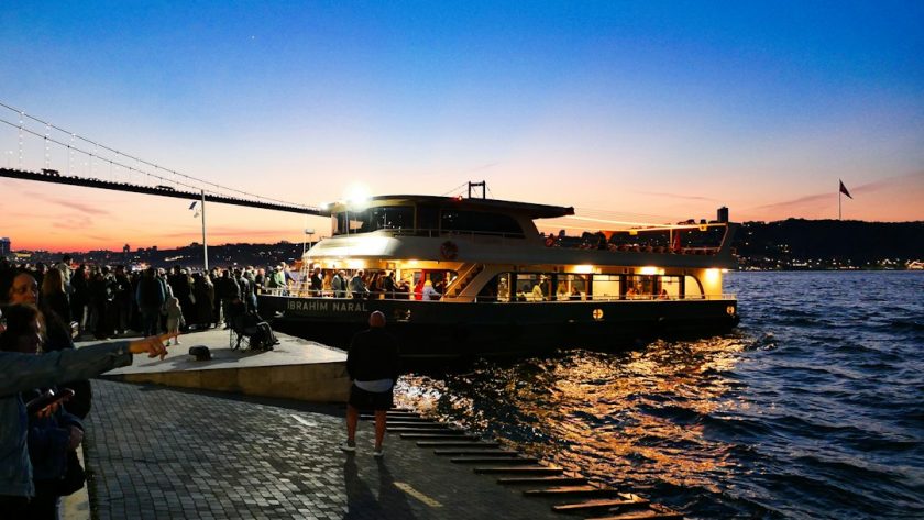 Ferry with lights sailing at dusk near a crowded dock
