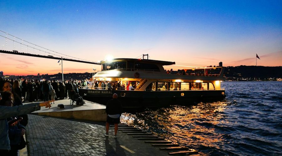 Ferry with lights sailing at dusk near a crowded dock