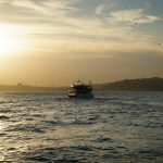 A boat sails on the water during a golden sunset
